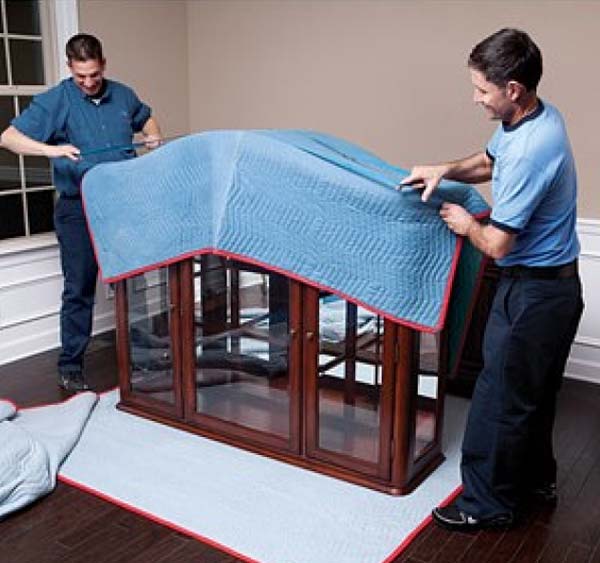 Two men in blue putting padding blankets on furniture